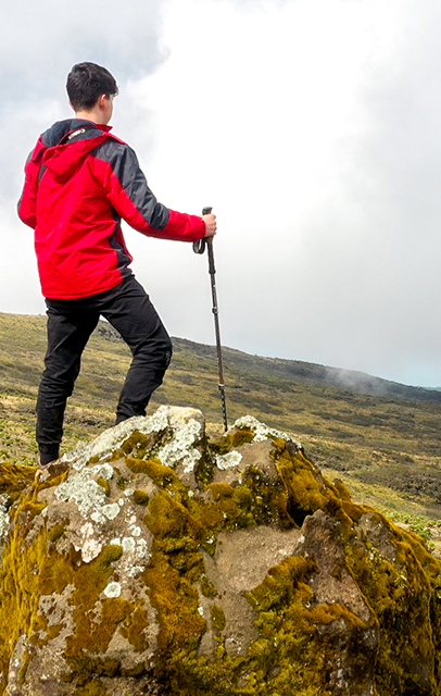 Hiker standing on a rocky mountain peak during a hiking adventure in Rwenzori Mountains National Park.